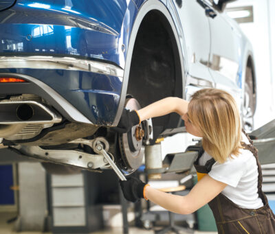 Process of changing tires of automobiles in auto service Process of changing tires of automobiles in auto service. Pretty female mechanic in coveralls standing under car and fixing machine in workshop. Concept of maintenance and repair process.