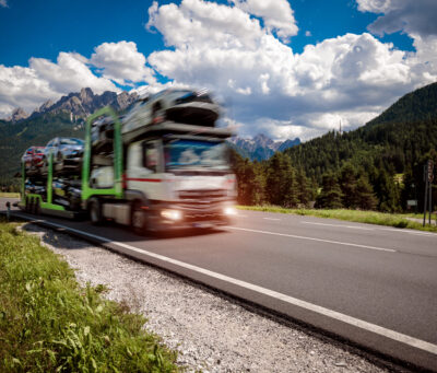 Truck trailer transports new cars rides on highway, Italy natural landscape Alps. Warning - authentic shooting there is a motion blur.